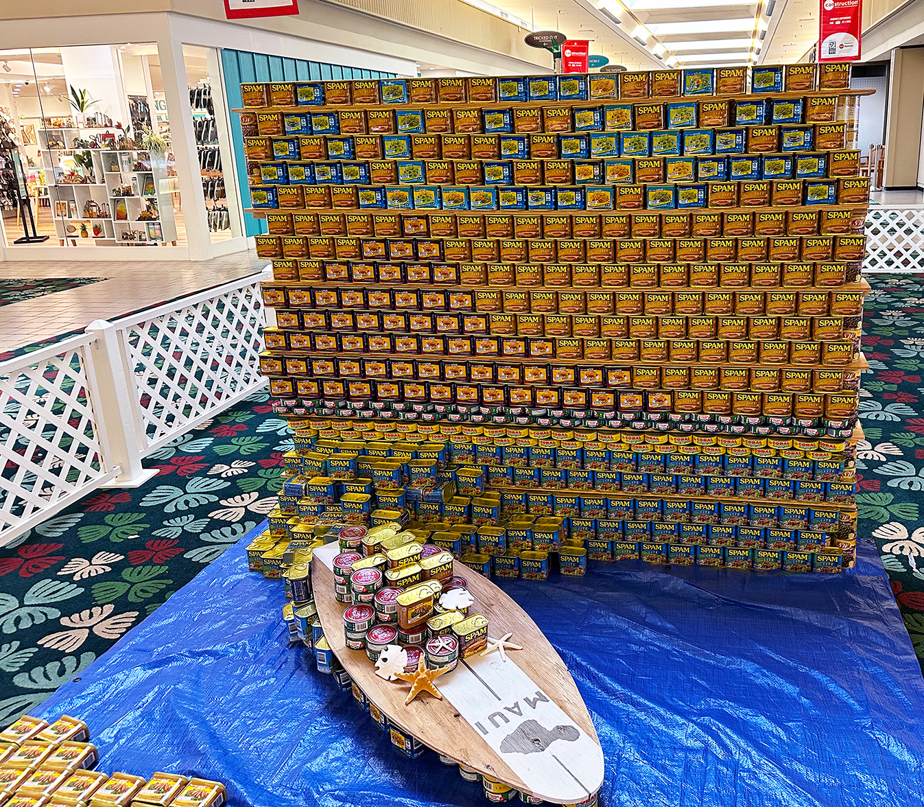 MGA's CANstruction Entry depicts a vintage postcard of Diamond Head at sunset (built out of cans of SPAM) with a 3-D depiction of a wave and surfboard carrying supplies to Ohana in need.